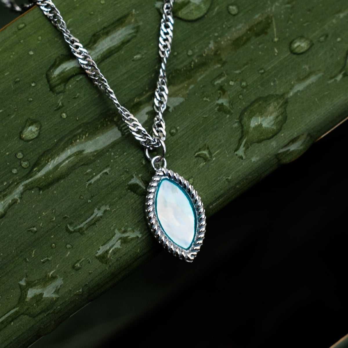 "Collana Visuale", un'elegante collana con dettagli in argento e nacre, su uno sfondo verde soffice.