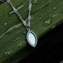 "Collana Visuale", un'elegante collana con dettagli in argento e nacre, su uno sfondo verde soffice.