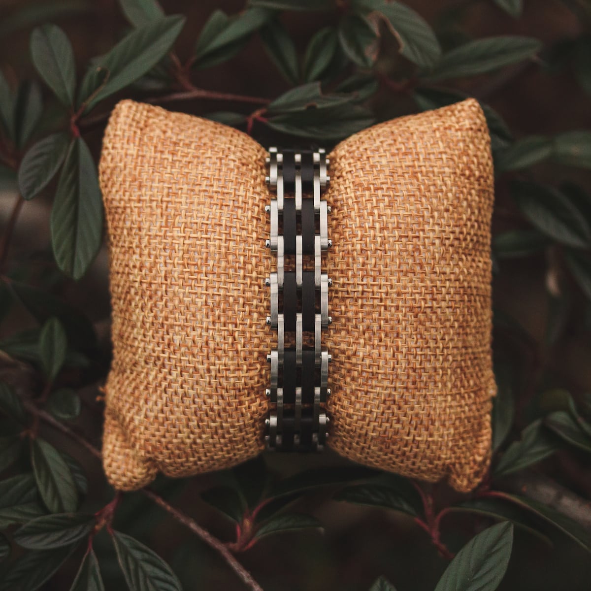 "Adagio", a stylish bracelet in maple and silver, displayed on a textured cushion among lush greenery.