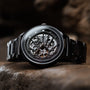 Orologio "Carbon" con acero grigio e grigio scuro, caratterizzato da un intricato meccanismo esposto.