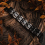 "Tremolo", un elegante bracciale in acero e grigio scuro, completa lo sfondo in legno rustico con eleganza naturale.
