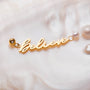 "Believe-Charm" fascino d'oro con perle, con un design "Believe" arricciante su un fondo morbido.