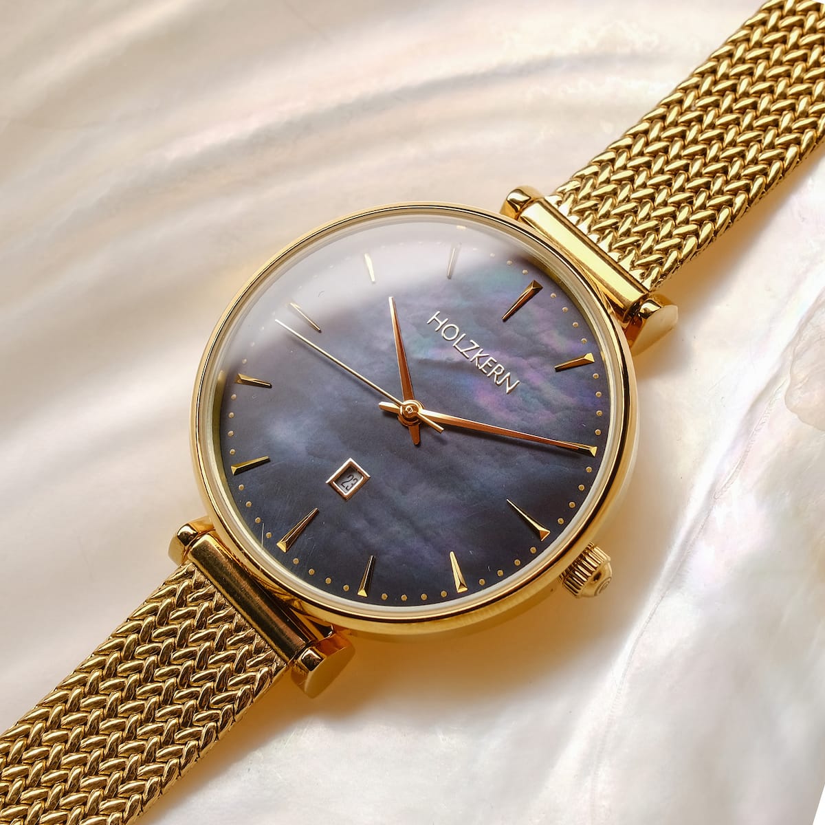 "Giggles", a stylish watch with a nacre dial and gold accents, featuring a woven metal strap for an elegant look.