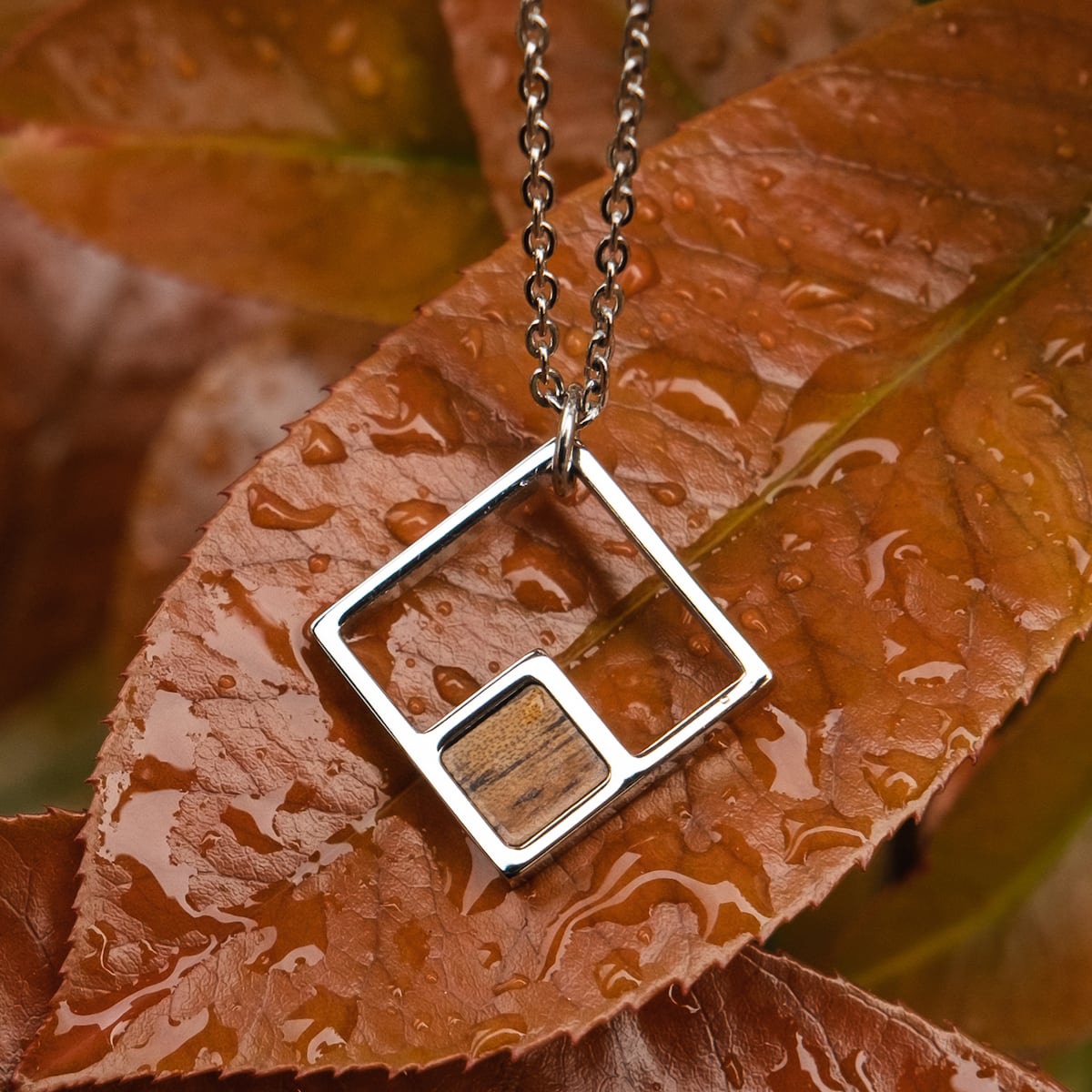 Collana "Geometrica" presenta un disegno geometrico in legno di Koa e argento, impostato contro le foglie di autunno.