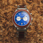 "Osprey watch, featuring a vibrant azure blue dial and koa wood accents, set against a natural background."