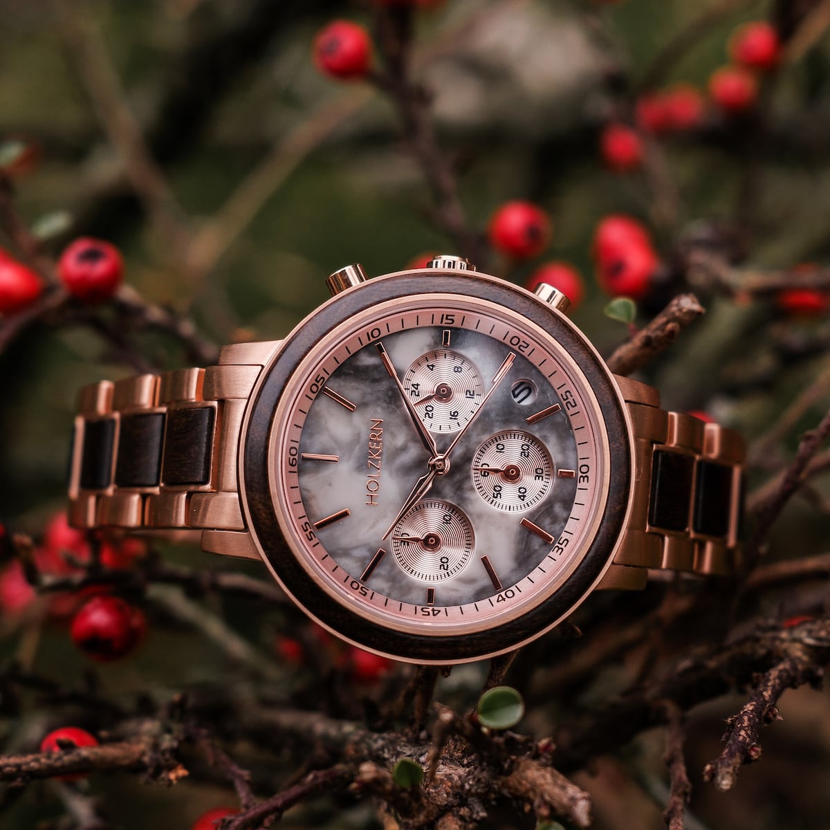 "Calina", elegante orologio da polso con dettagli in acero e marmo, impostato su uno sfondo naturale con accenti rossi vivaci.