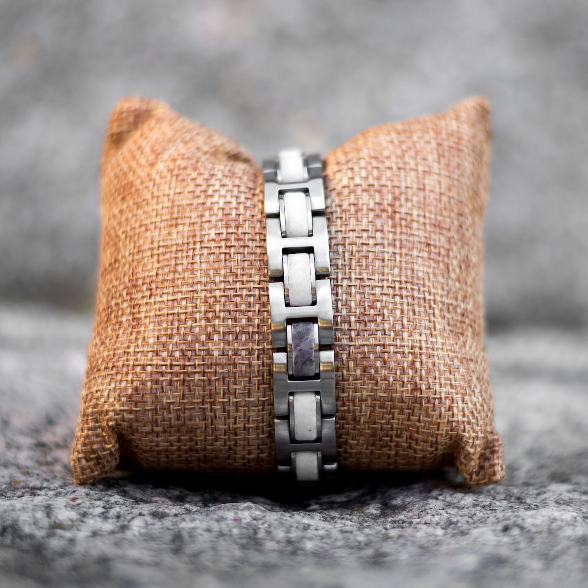 "Forte", a sophisticated marble and silver bracelet, displayed elegantly on a rustic woven cushion.