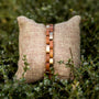 "Rondo", stylish bracelet in cherry and rose gold hues on woven cushion.