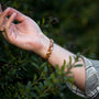 "Rondo" bracelet in cherry and rose gold with a sleek, elegant design amidst green foliage.