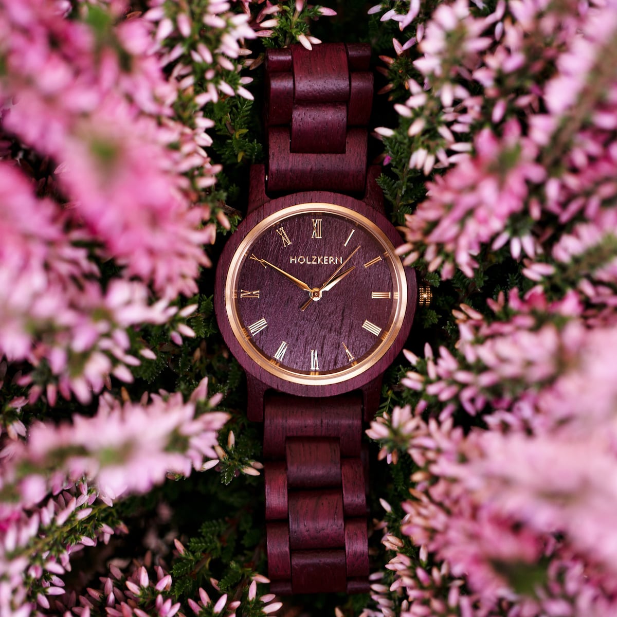 Orologio in legno "Calm" con un elegante design amaranto circondato da fiori rosa.