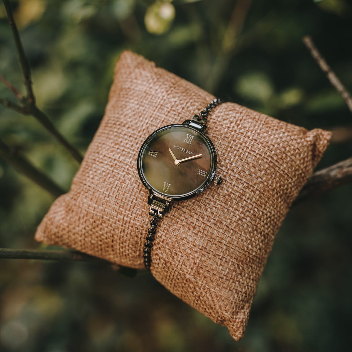 Orologio "Élisa" con quadrante a forma di nacre e accenti grigio scuro su un cuscino in frusta rustico.