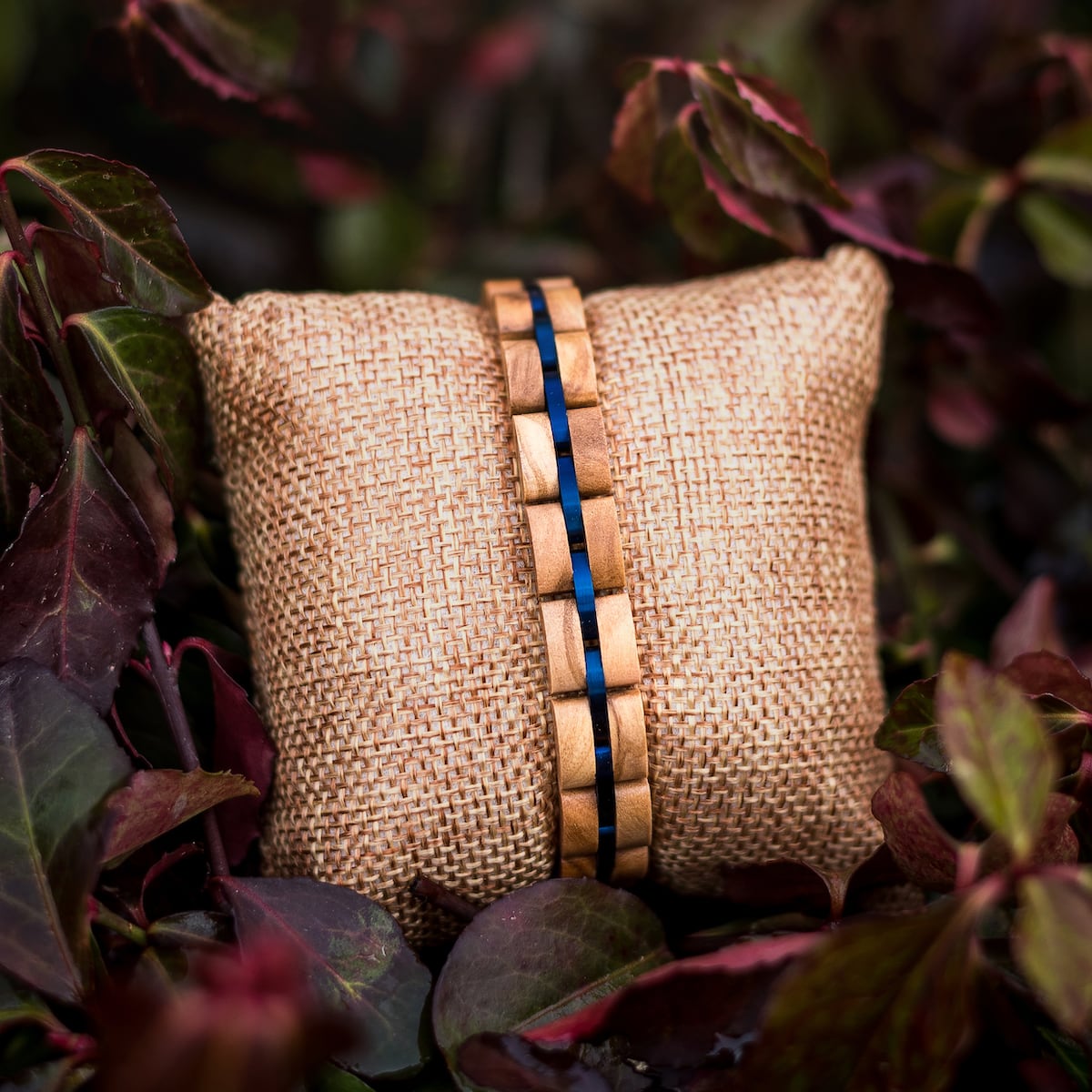 Bracciale "Fantasia" realizzato con ulivi e accenti blu, presentato su frusta in mezzo fogliame.