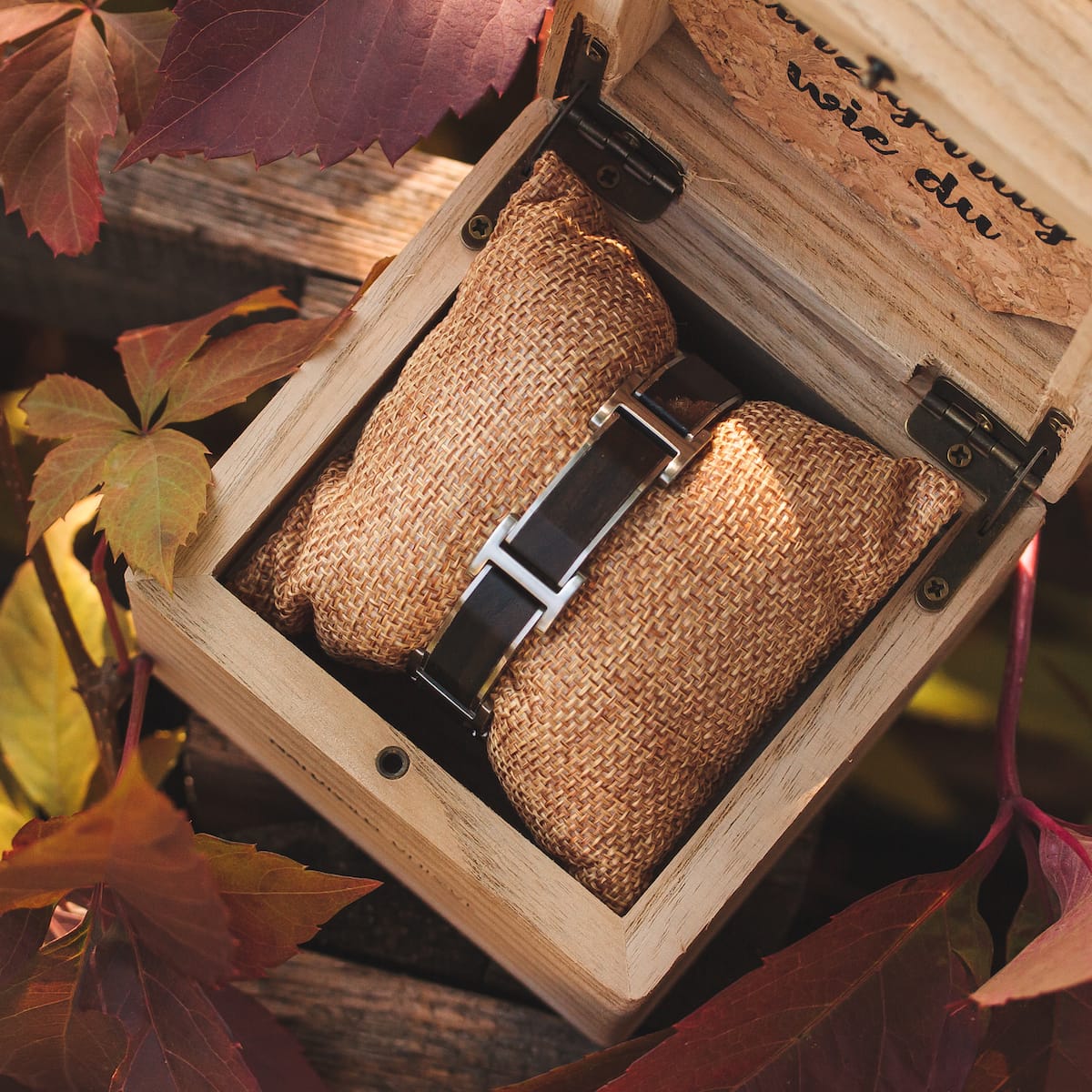 Orologio "Acapella", con un design in legno di piombo e argento, incastonato in una scatola rustica con foglie autunnali.