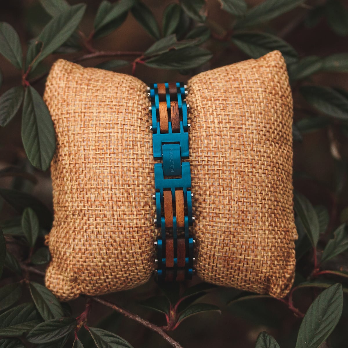 "Adagio" wristwatch, featuring Koa wood and blue accents, displayed on a textured cushion with foliage backdrop.