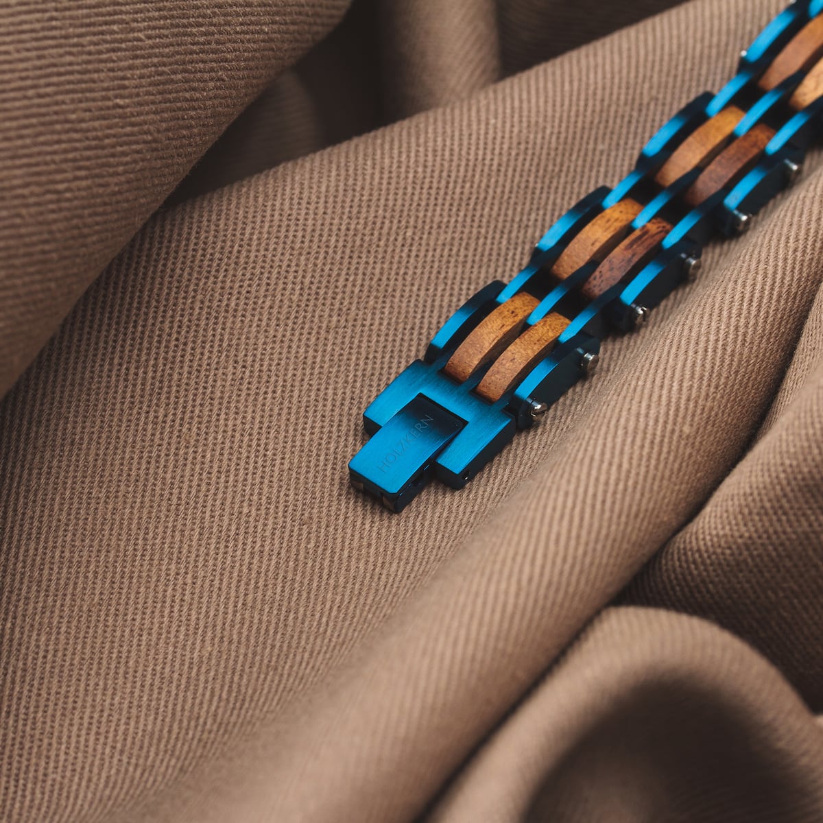 "Adagio" bracelet featuring koa wood and vibrant blue links on textured fabric backdrop.