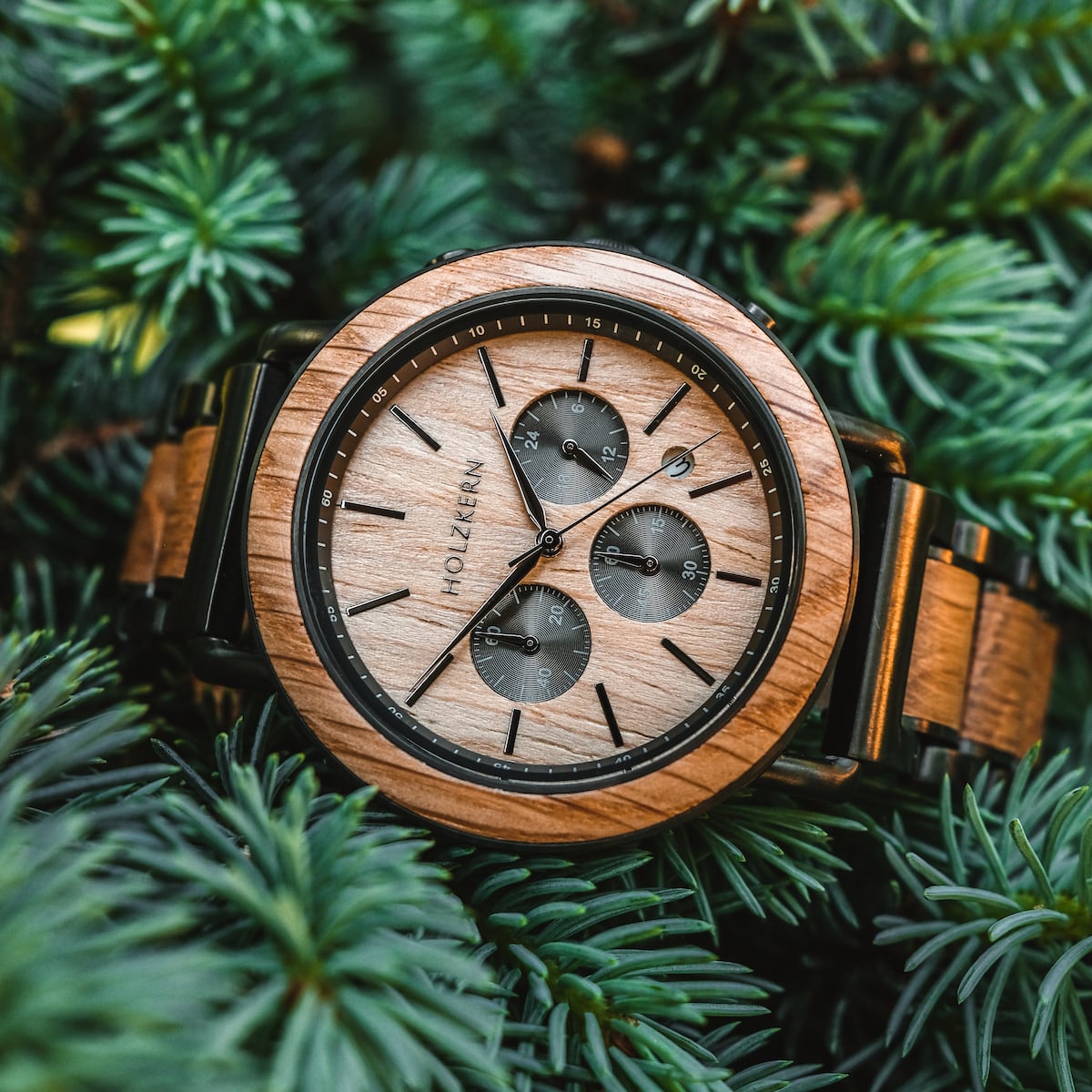 "Whakaari" watch featuring an oak dial and band, set against lush green foliage.