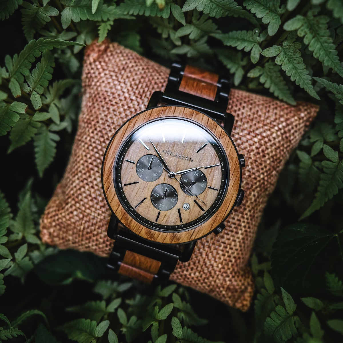 "Whakaari" watch with oak finish, featuring a classic chronograph design nestled on a cushion among ferns.
