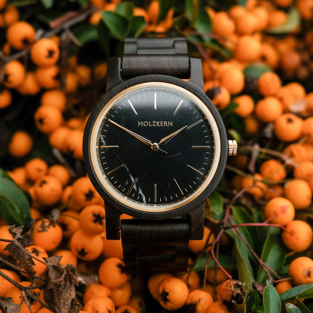 Orologio "Summer Night" con un elegante viso nero e una fascia di acero ambientata sullo sfondo di vivaci bacche arancione.