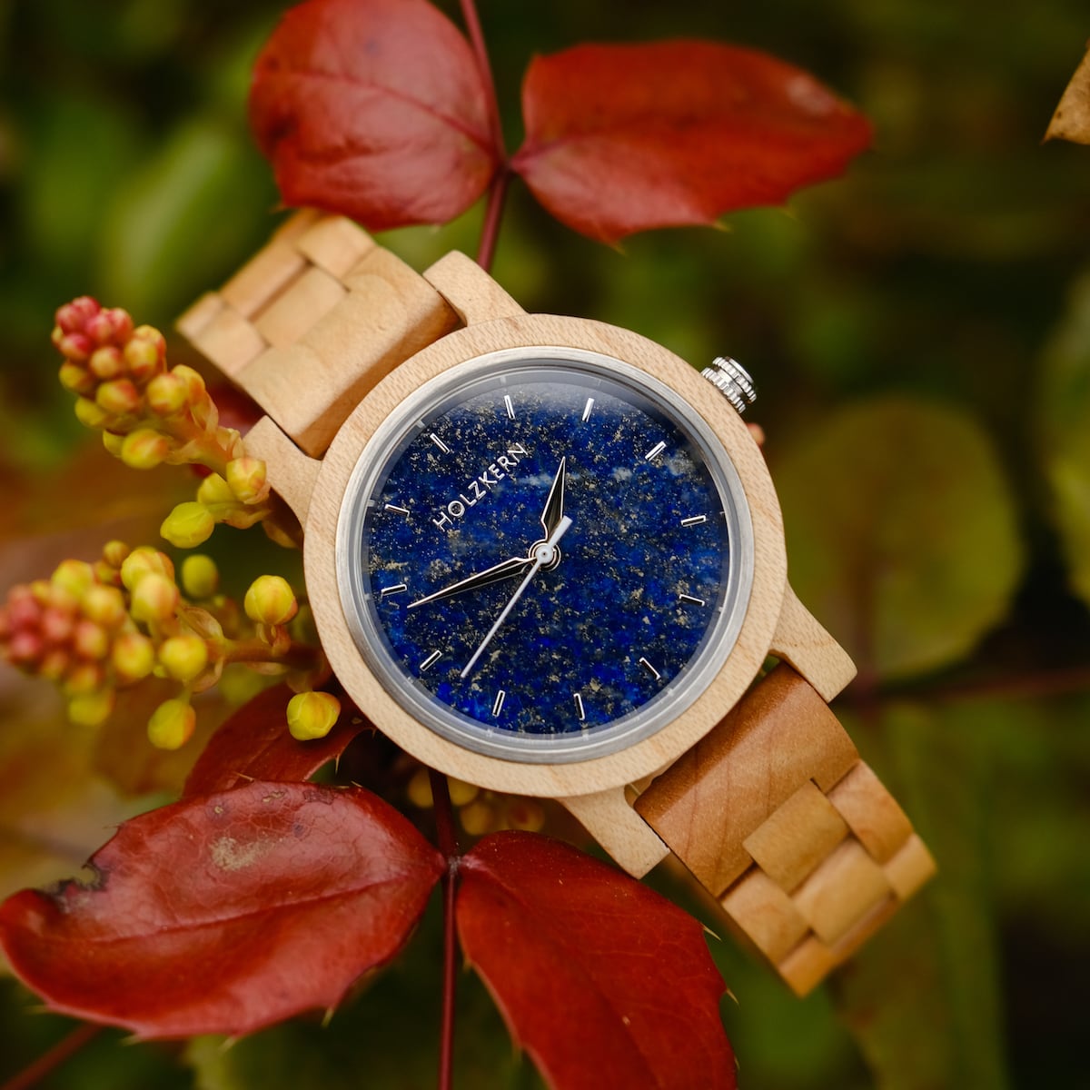 Orologio da polso in legno "Water" con cornice acerole e quadrante lapis lazuli, ambientato su uno sfondo di foglie autunnali.