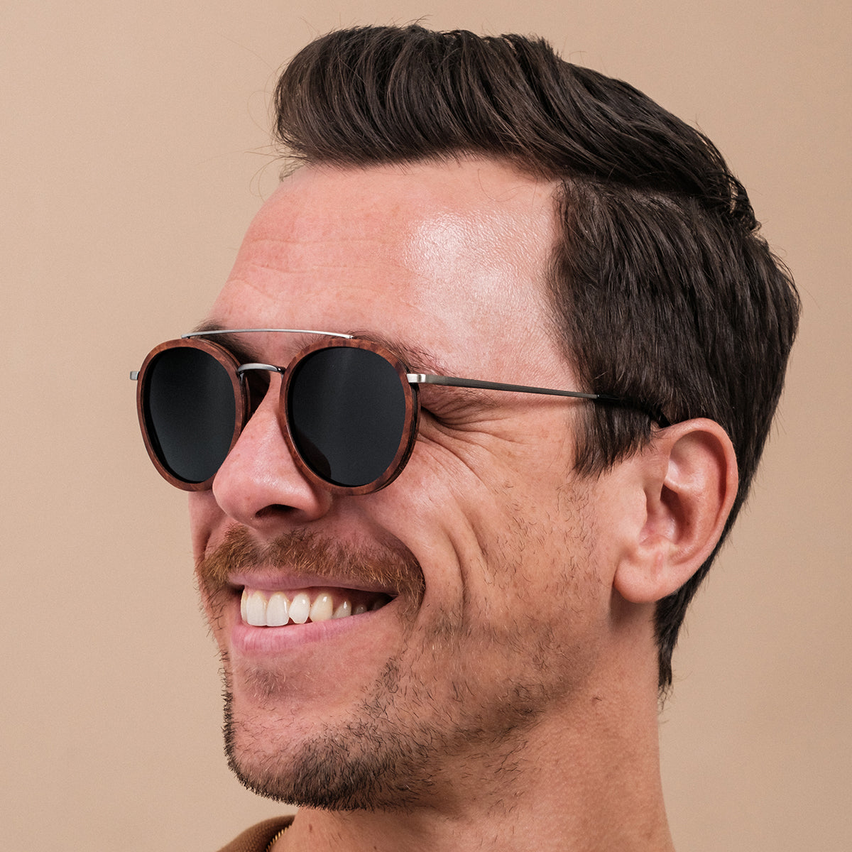 Occhiali da sole "Incanto" con uno stile in noce e argento antico, indossati da una persona sorridente.