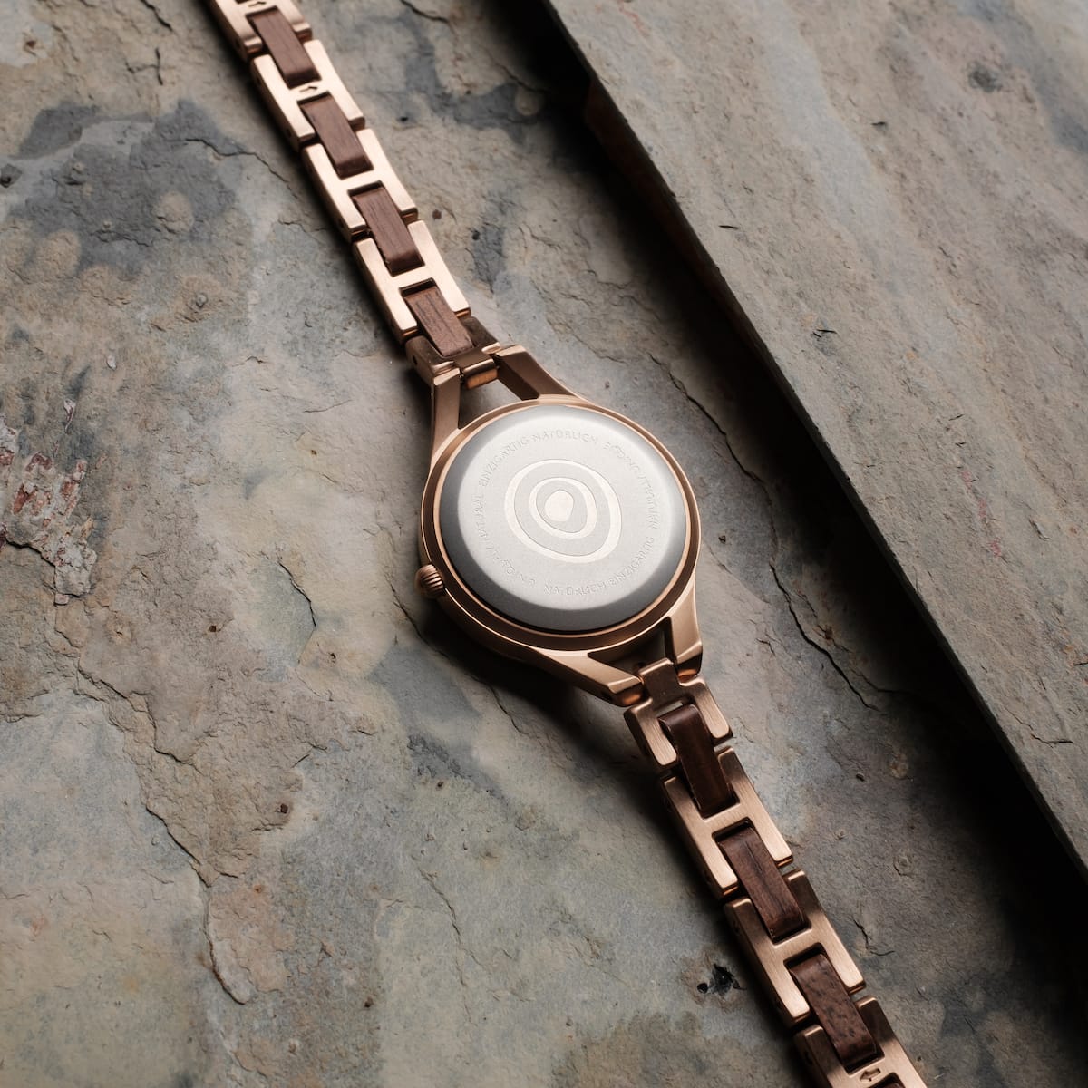"Fatima" watch featuring walnut and nacre materials with a sophisticated design on a textured surface.