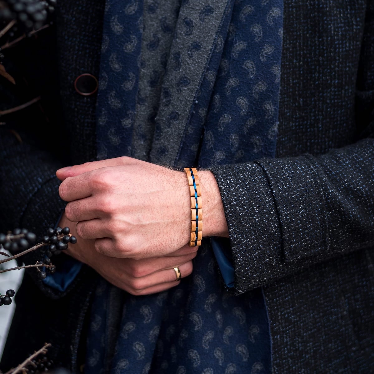 Bracciale "Fantasia" con un elegante legno di ulivo e un design blu su un polso su un fondo di giacca scura strutturato.