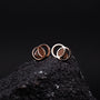 Orecchini effigi in oro noce e rosa con un design moderno e circolare su uno sfondo scuro texture.