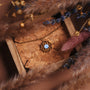 Collana "Composition Collana" con un pendente blu nacre in oro, esposto su uno sfondo rustico con accenti naturali.
