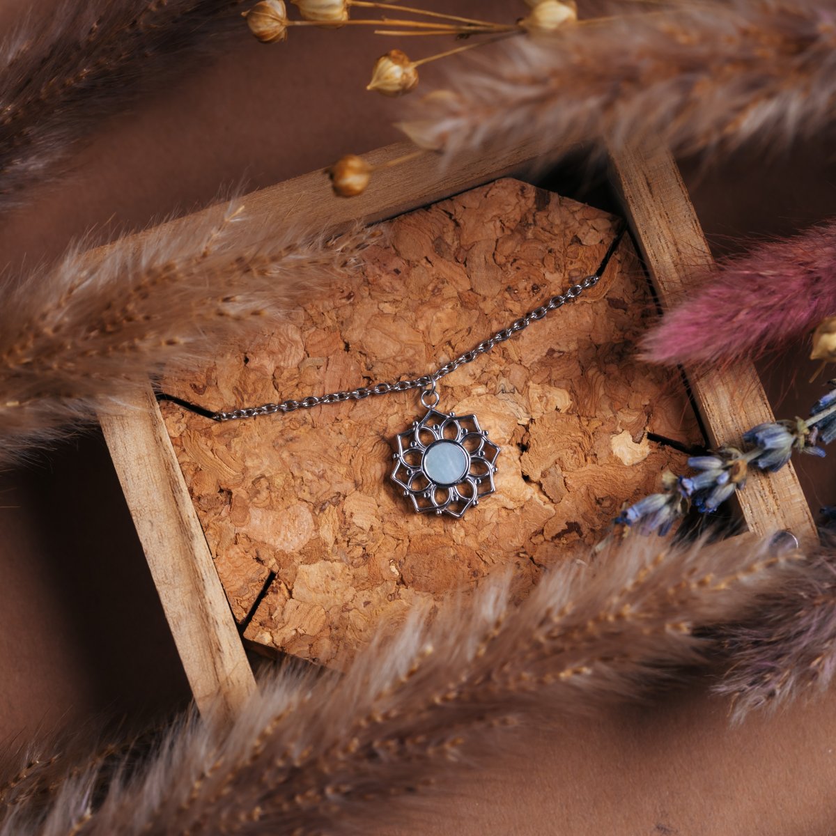 "Composition Necklace", a silver necklace featuring a white nacre pendant with an intricate design, lies stylishly in a rustic setting.