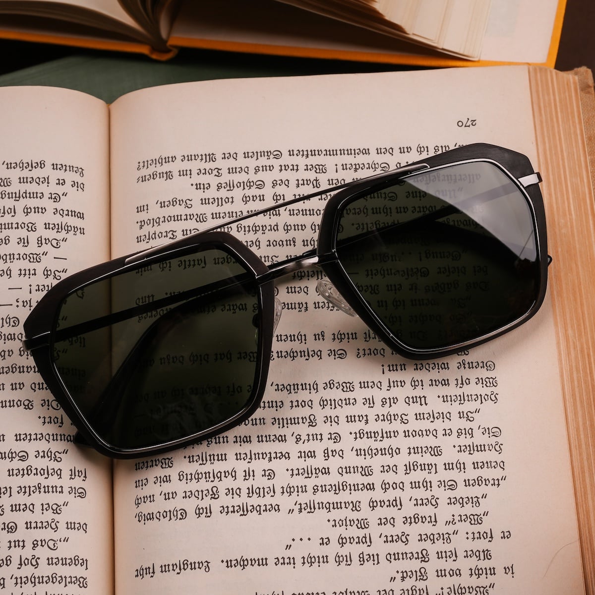 "The Storyteller sunglasses, featuring a Leadwood and Antique Silver style, elegantly resting on an open book."