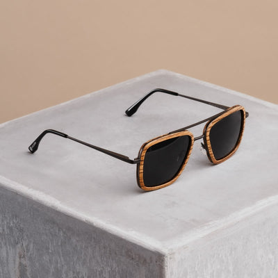 "The Logician" sunglasses featuring a zebrawood frame and dark grey lenses on a concrete surface.