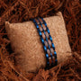 "Kanon" bracelet in walnut and blue, showcasing a sleek, modern design on a textured cushion background.