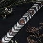 "Prelude", un elegante bracciale con dettagli in noce e argento, impostato su uno sfondo scuro con accenti floreali.