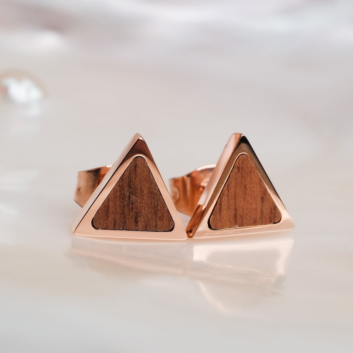 "Scheale orecchini" sono orecchini triangolari con accenti in legno di noce e oro rosa, che offrono uno stile elegante e moderno.