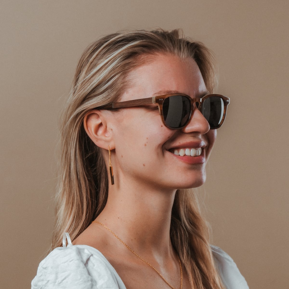 "The Comedian" sunglasses, featuring a stylish walnut and honey finish, worn by a smiling person.