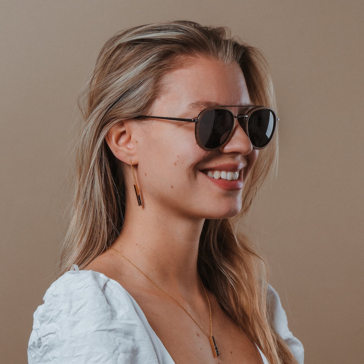 "The Risky" sunglasses in walnut and dark grey, featuring a sleek and modern style worn by a smiling individual.