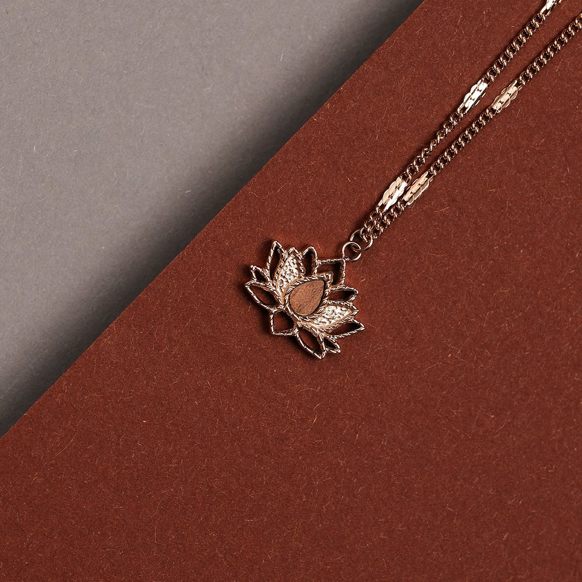 "Collana di danza", una collana in noce e oro rosa con un ciondolo di loto, in stile su uno sfondo marrone e grigio.