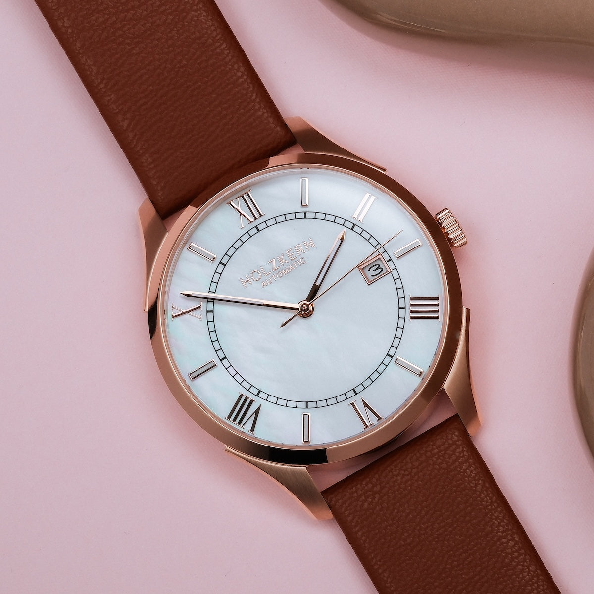 "Milestones" watch with nacre face and brown strap, featuring elegant Roman numerals and a polished finish.