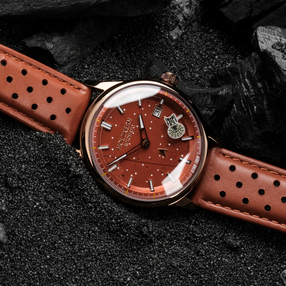 L'orologio "NCC-1701-D" presenta un quadrante a jasper-red con dettagli eleganti e un cinturino in pelle perforato.
