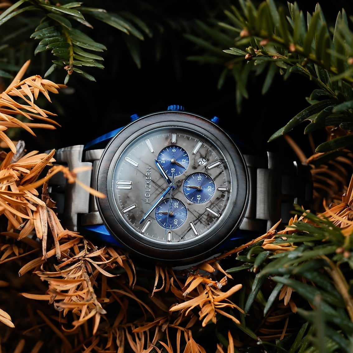 "Intergalactic watch featuring a marble face and leadwood accents, nestled among pine branches."