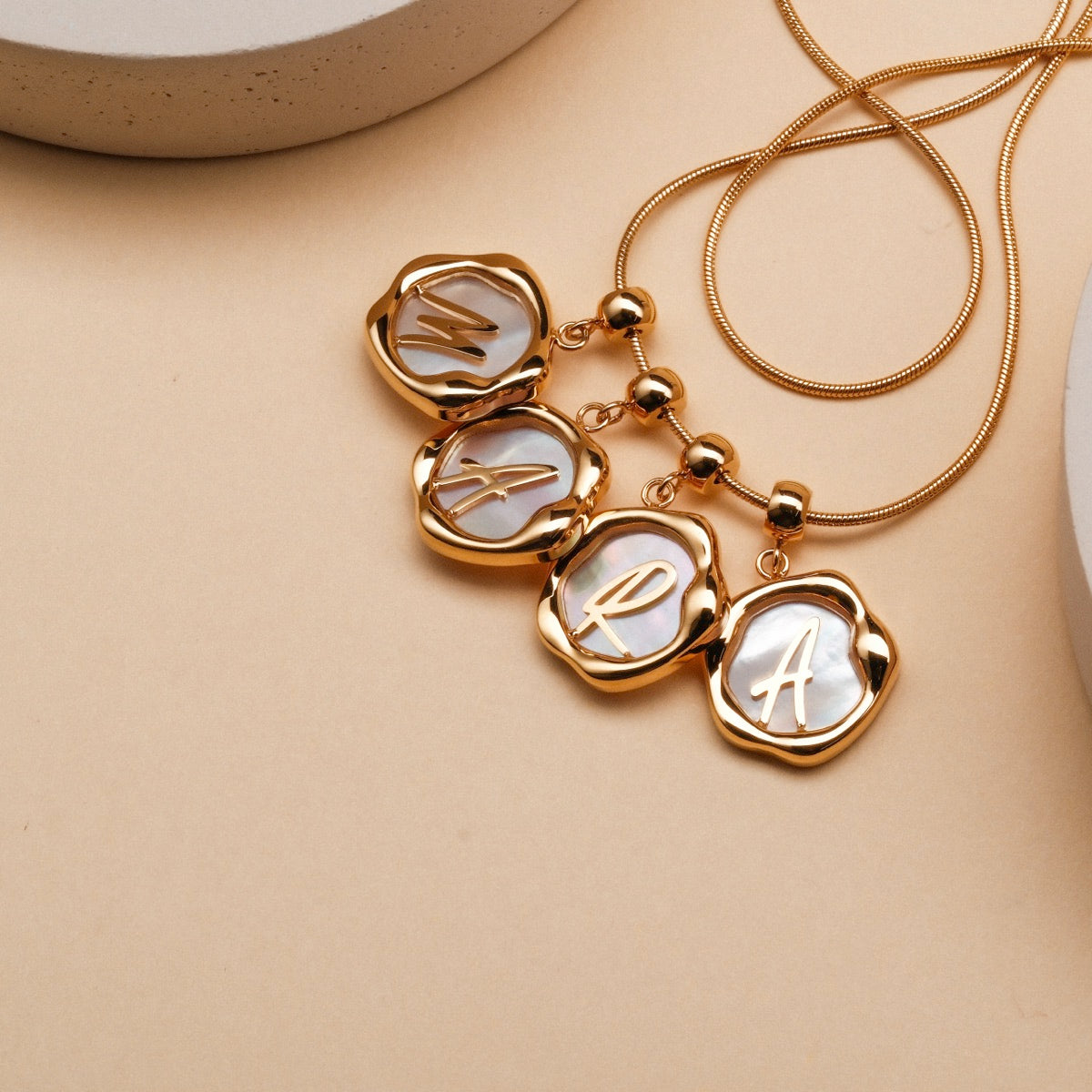 "Letter Charm A-Z" lettera charms con accenti d'oro, visualizzati su una catena delicata.
