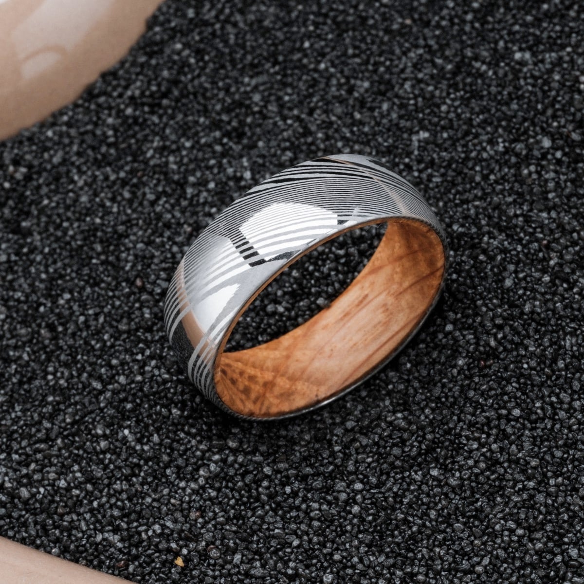 "Sumo Ring" ring featuring a sleek design with oak wood interior and Damascus steel exterior, set against a dark textured background.
