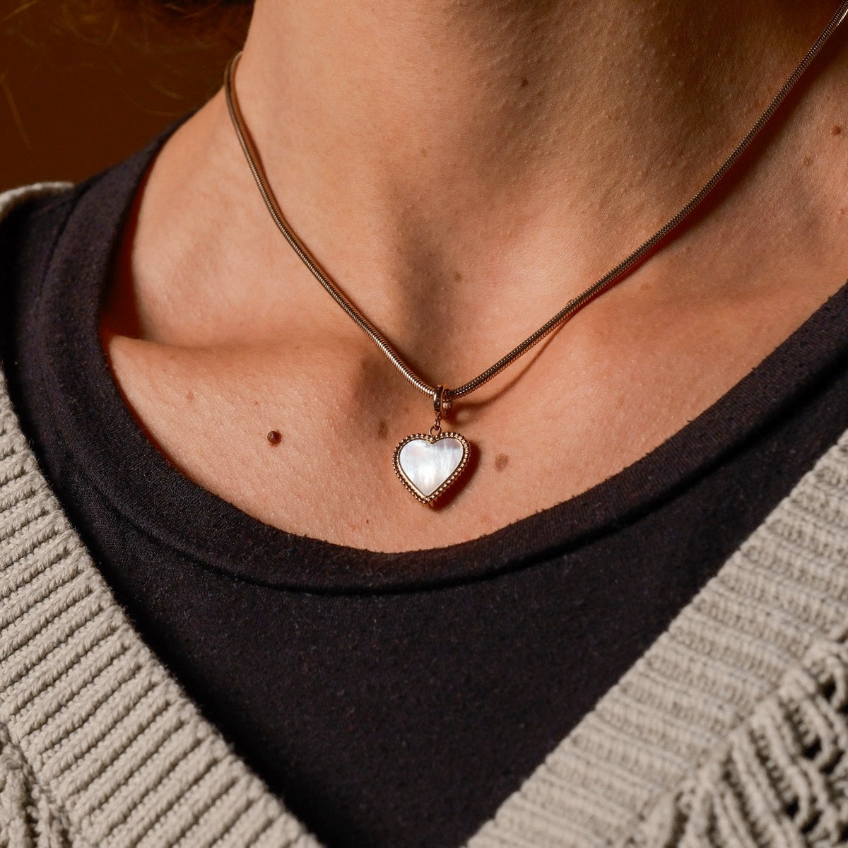 Collana a forma di cuore "Amorance Collana" con un pendente intarsiato e dettagli in oro rosa, indossato su un maglione con texture e top nero.