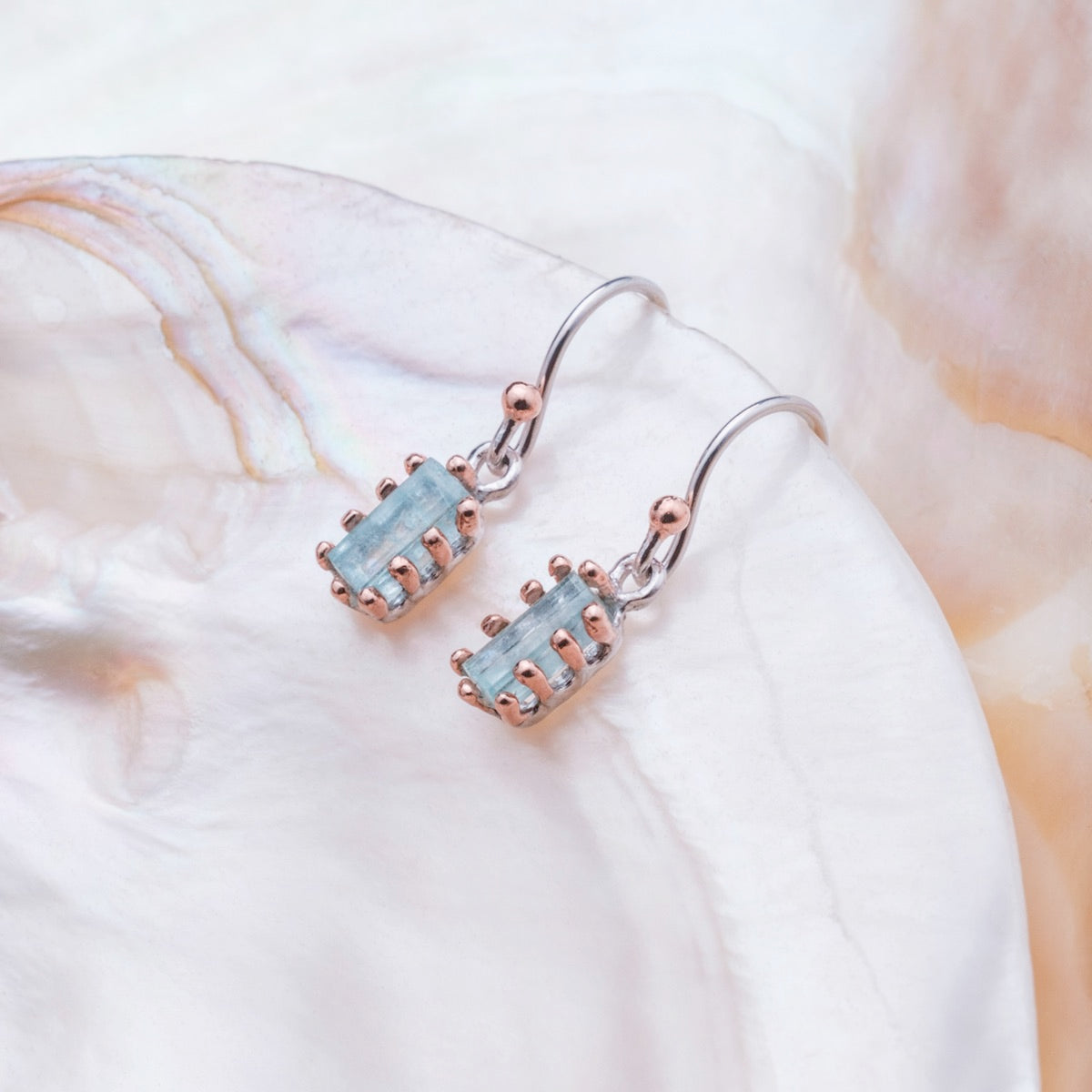 "Silverstream Earrings, elegant earrings featuring aquamarine and rosegold accents, set against a pearlescent background."