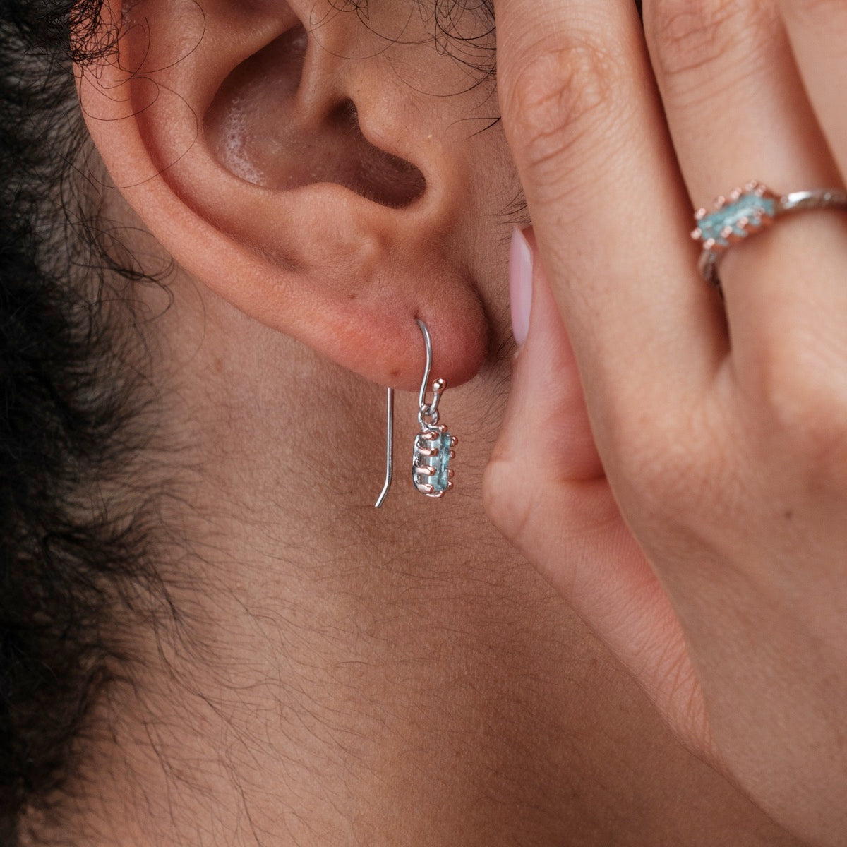 "Silverstream Earrings earrings, featuring aquamarine stones and rosegold accents, displayed on an ear for elegant style."