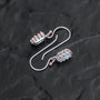 "Silverstream Earrings, elegant earrings with aquamarine stones and rosegold accents, on a dark textured surface."