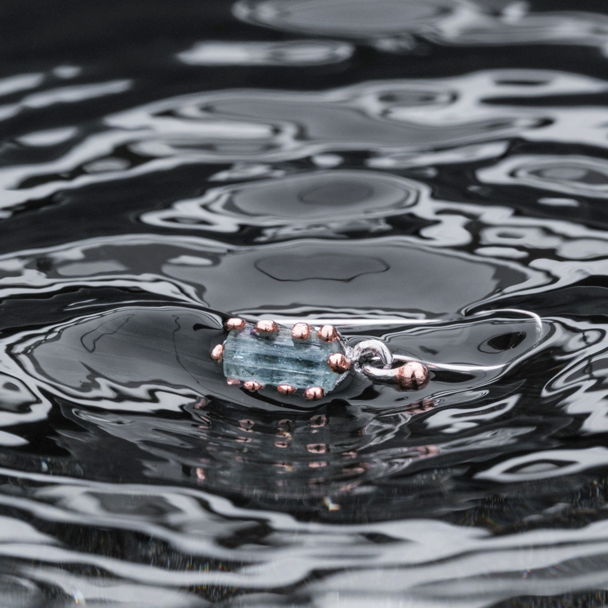 "Silverstream Earrings, elegant earrings in aquamarine and rosegold, showcased on rippling water for a serene touch."