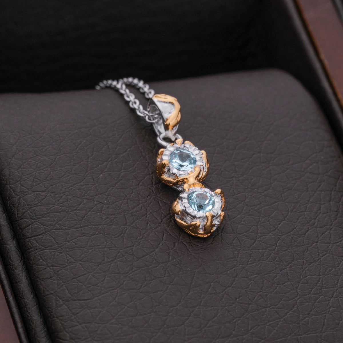 Collana "Silverstream", con un design in oro elegante con pietre tomatiche, elegantemente esposta su un fondo in pelle scura.