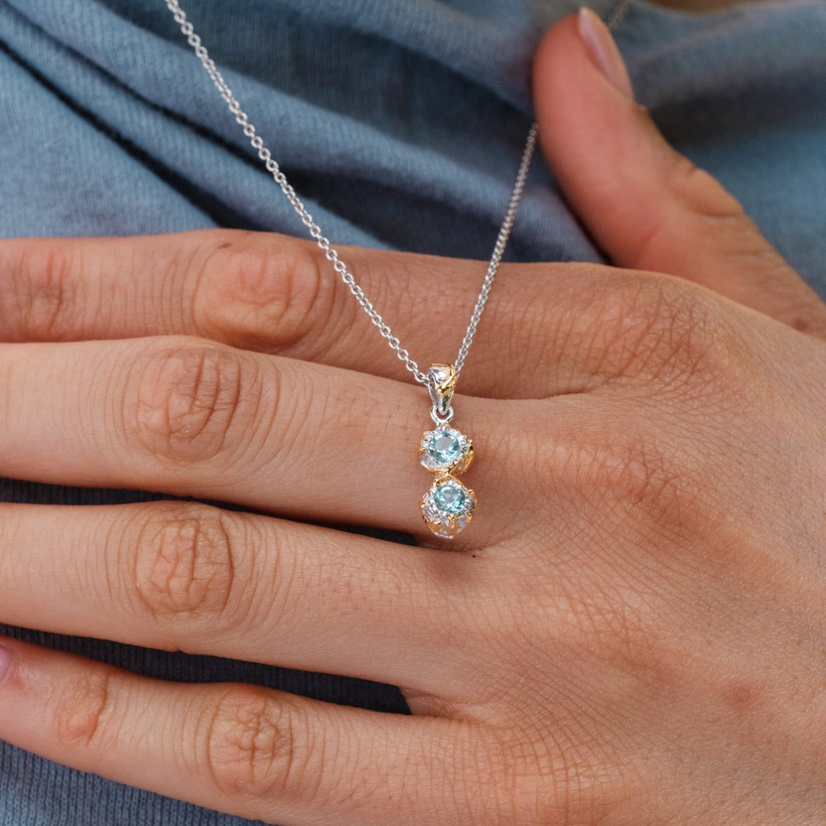 "Collana argentata": Elegante collana con pietre a topane in oro, indossata intorno al collo su uno sfondo di tessuto blu.