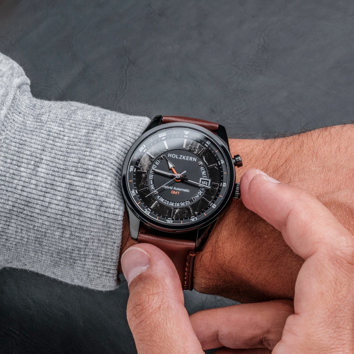 "Gmt Skywhirl" watch with marble and black dial, brown leather strap, worn on wrist.
